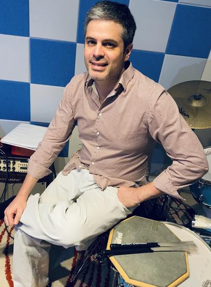 Photo of Juan Francisco Megna, seated next to a drum kit in front of a colorfully painted wall.